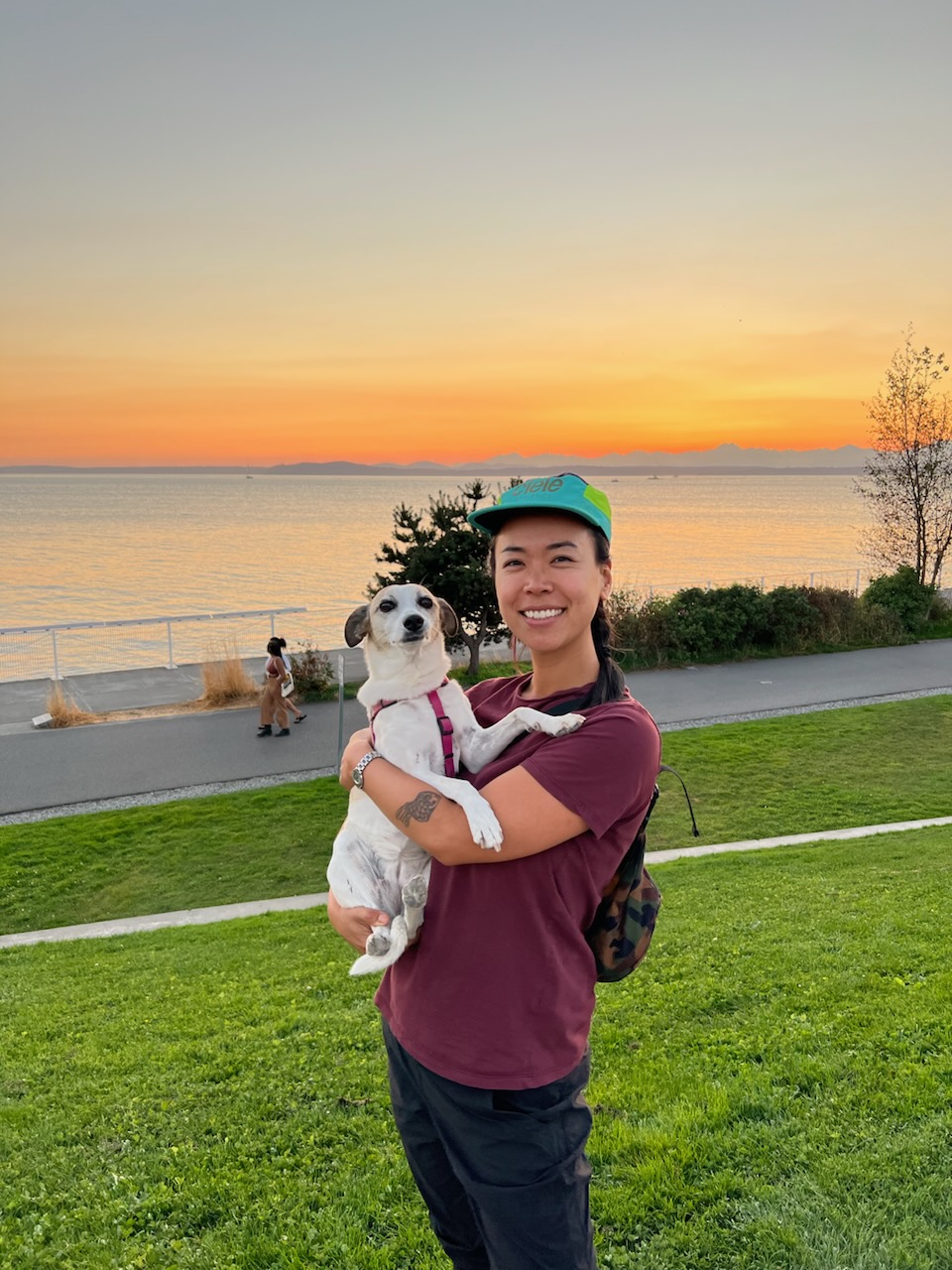 Bin Jung wth dog Concha in her arms in front of a sunset on water.